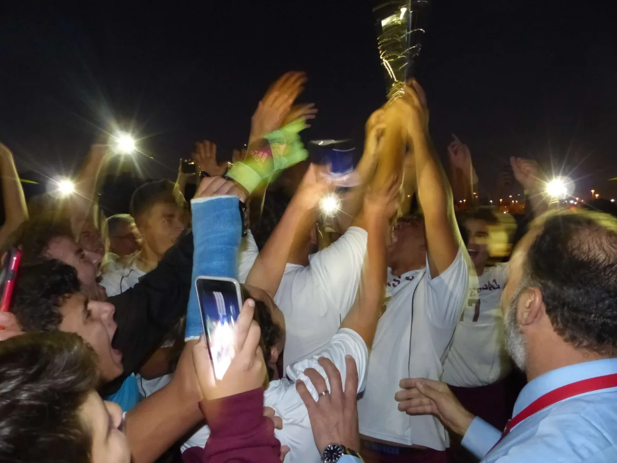 Universal School students lifting a gold trophy under stadium lights at night